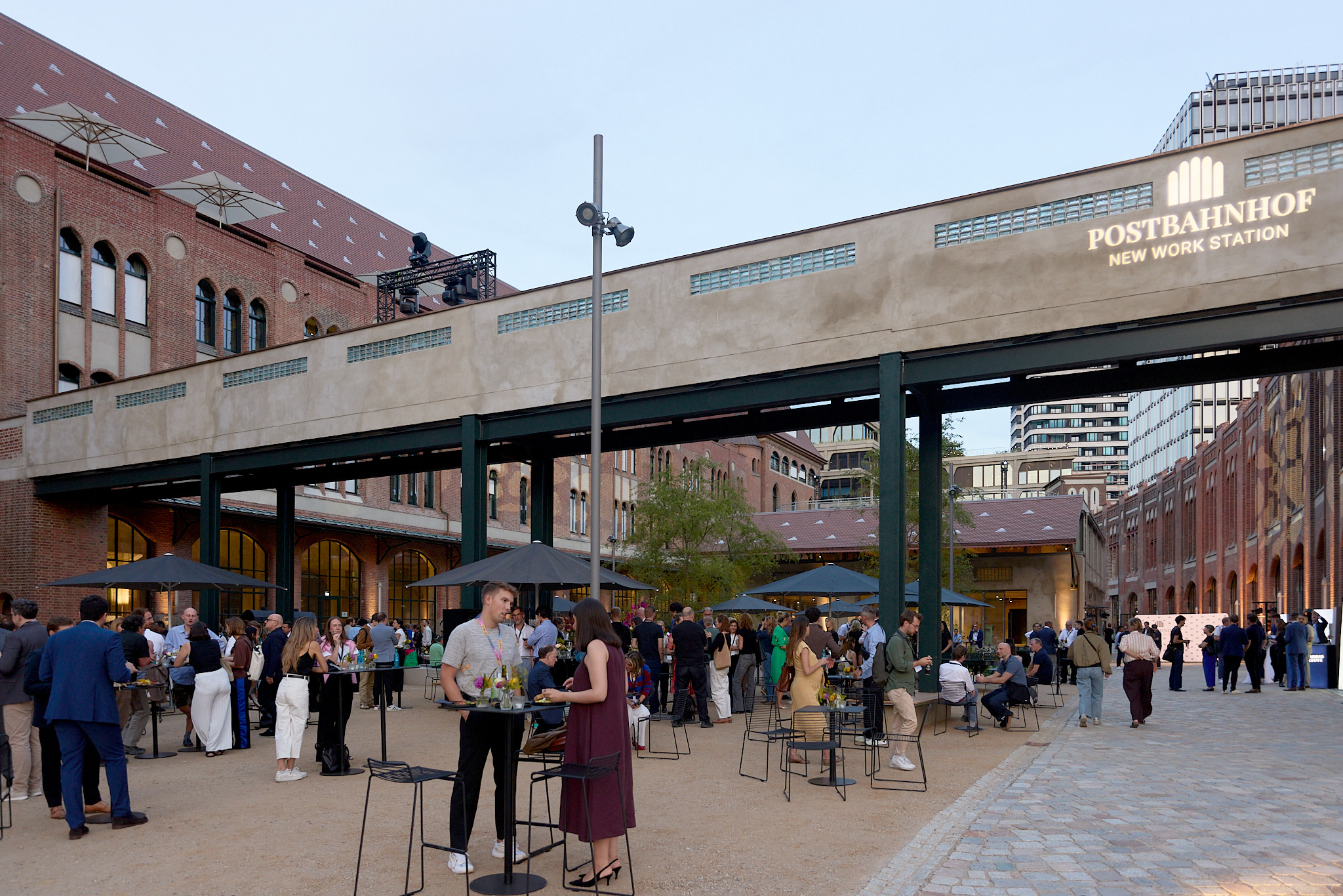Sommerfest im Outdoor Office des Postbahnhofs Berlin mit zahlreichen Gästen unter der historischen Verbindungsbrücke.