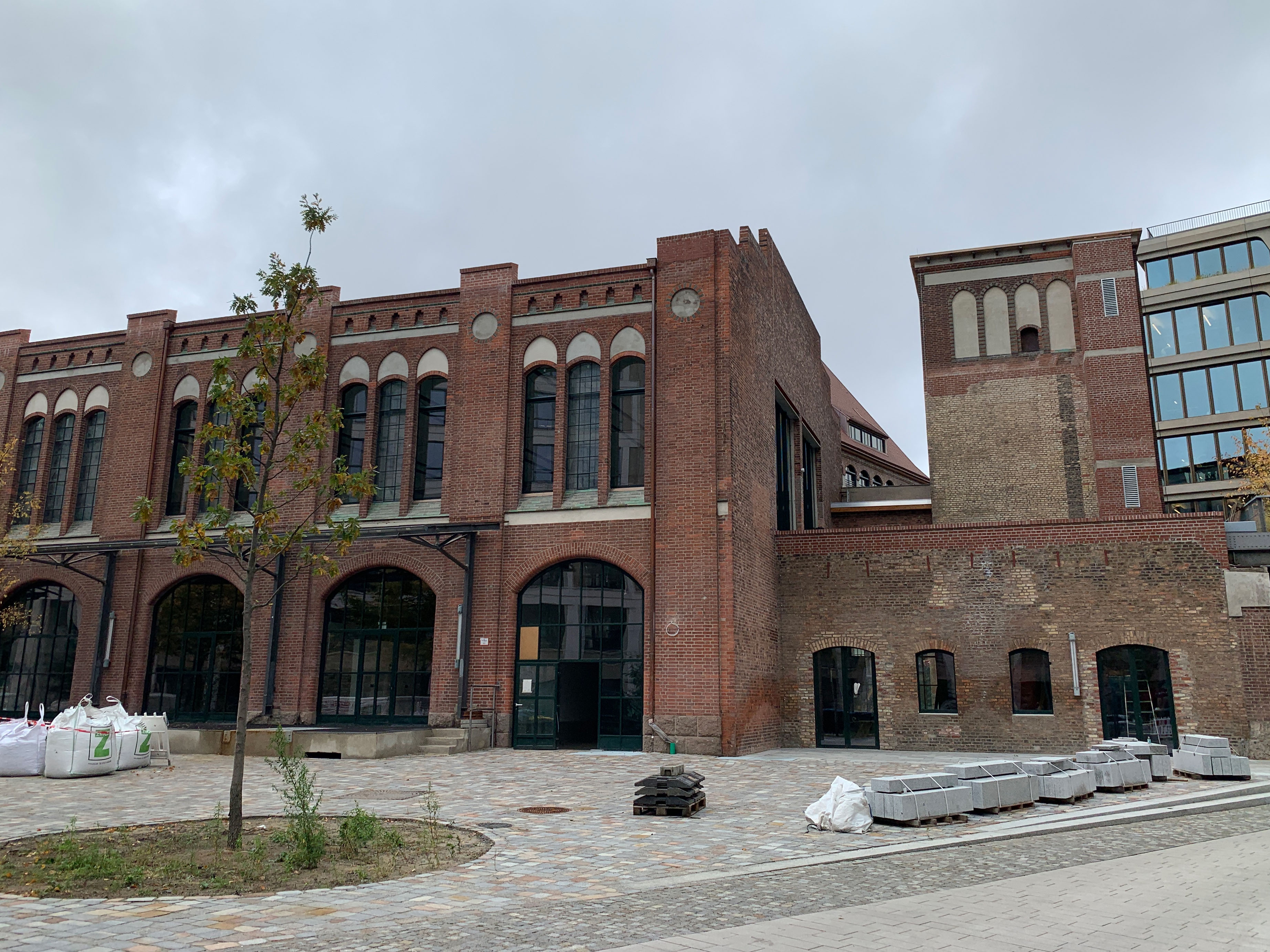 postbahnhof-offices-berlin-baufortschritt-aussenansicht-eingangspackkammer Backsteingebäude mit großen Rundbogenfenstern und gepflastertem Vorplatz, Ansicht der ehemaligen Packkammer von außen.