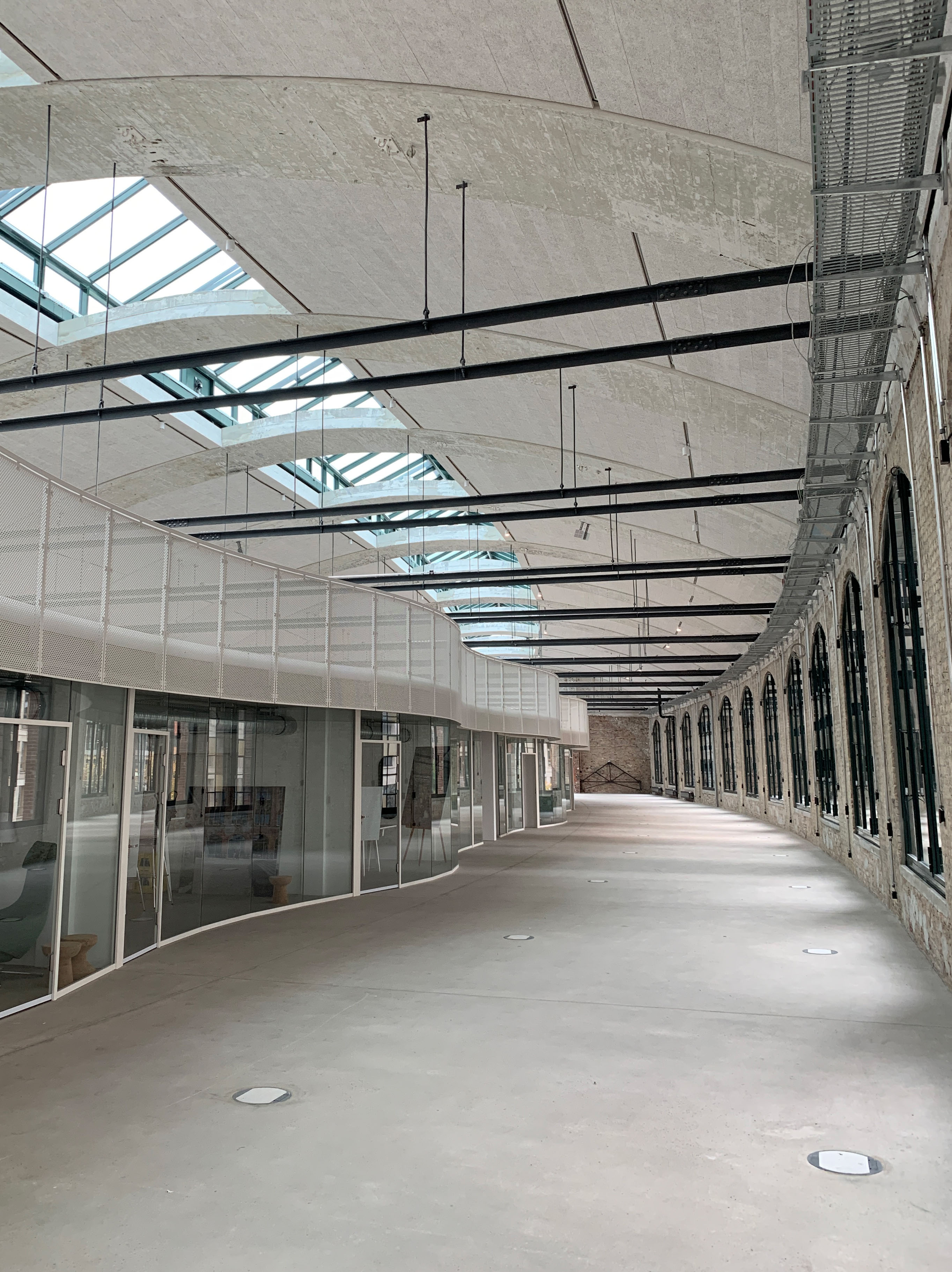 postbahnhof-offices-berlin-baufortschritt-eingangspackkammer_Image (15) Großer lichtdurchfluteter Flur mit Glasfassaden und abgehängter Decke, Blick entlang der geschwungenen Architektur.