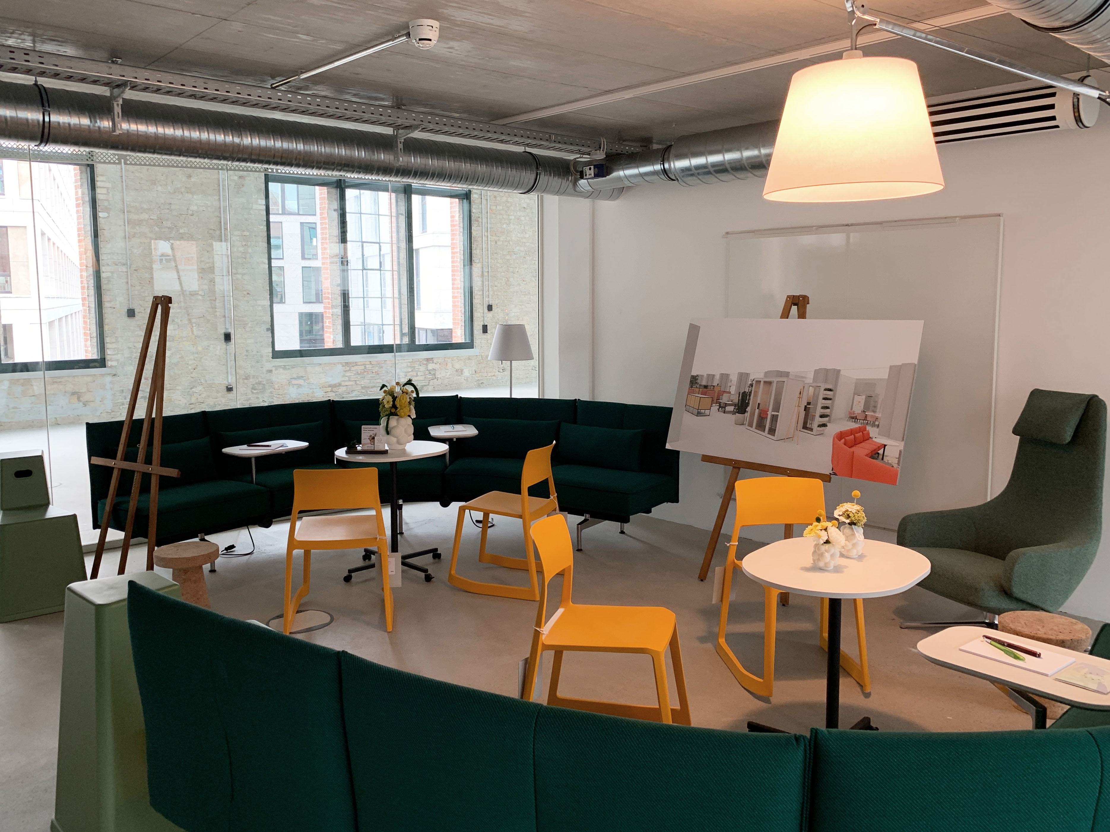 postbahnhof-offices-berlin-baufortschritt-musterbüro_Image (28) Gemütliche Lounge mit grünen Sofas und gelben Stühlen, eingerichtetem Besprechungsbereich mit Modelltafeln und Stehleuchten.