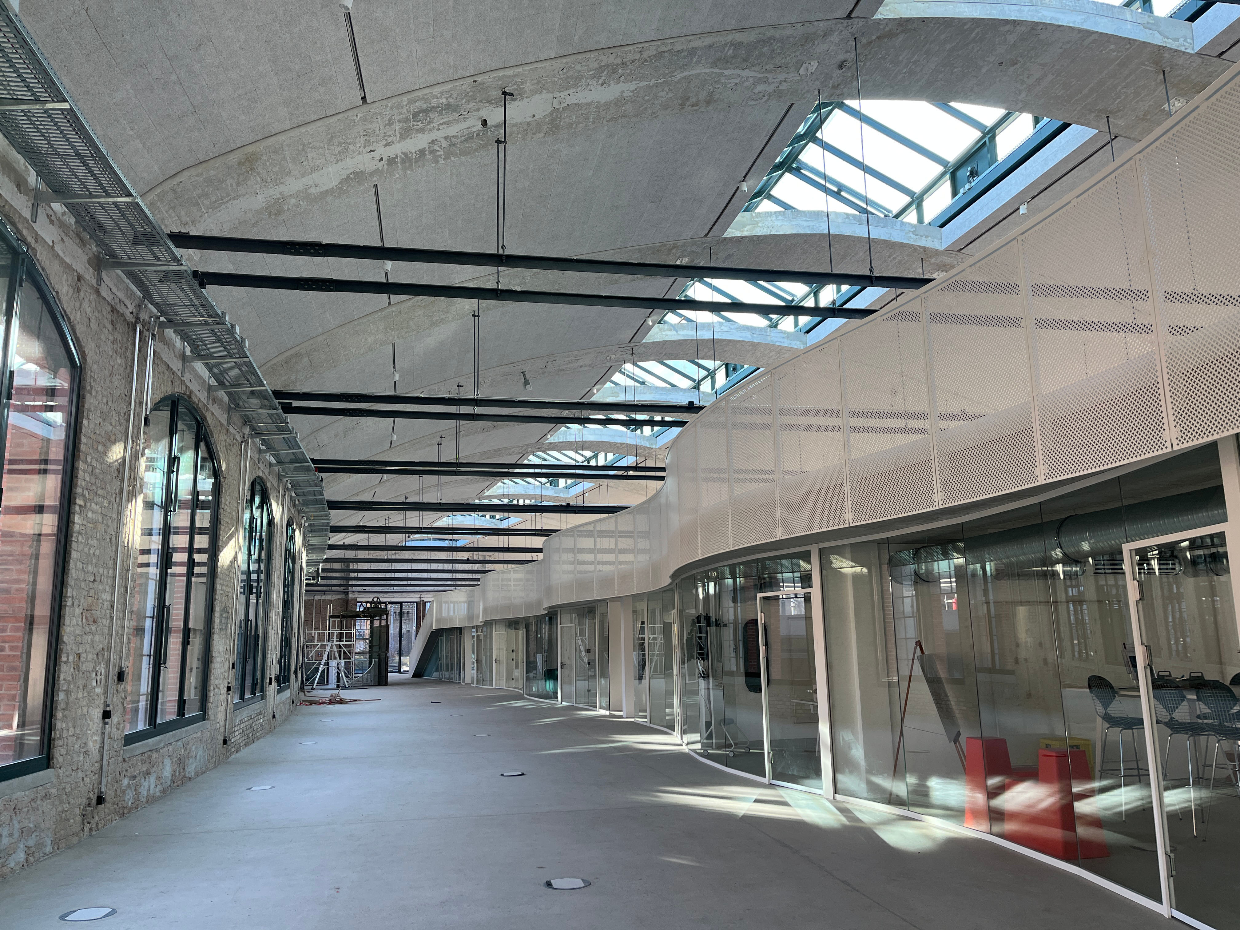 Außenansicht des Baufortschritts im Postbahnhof Berlin mit Blick in den modernen Innenbereich mit Glasfronten und Gewölbedecke.