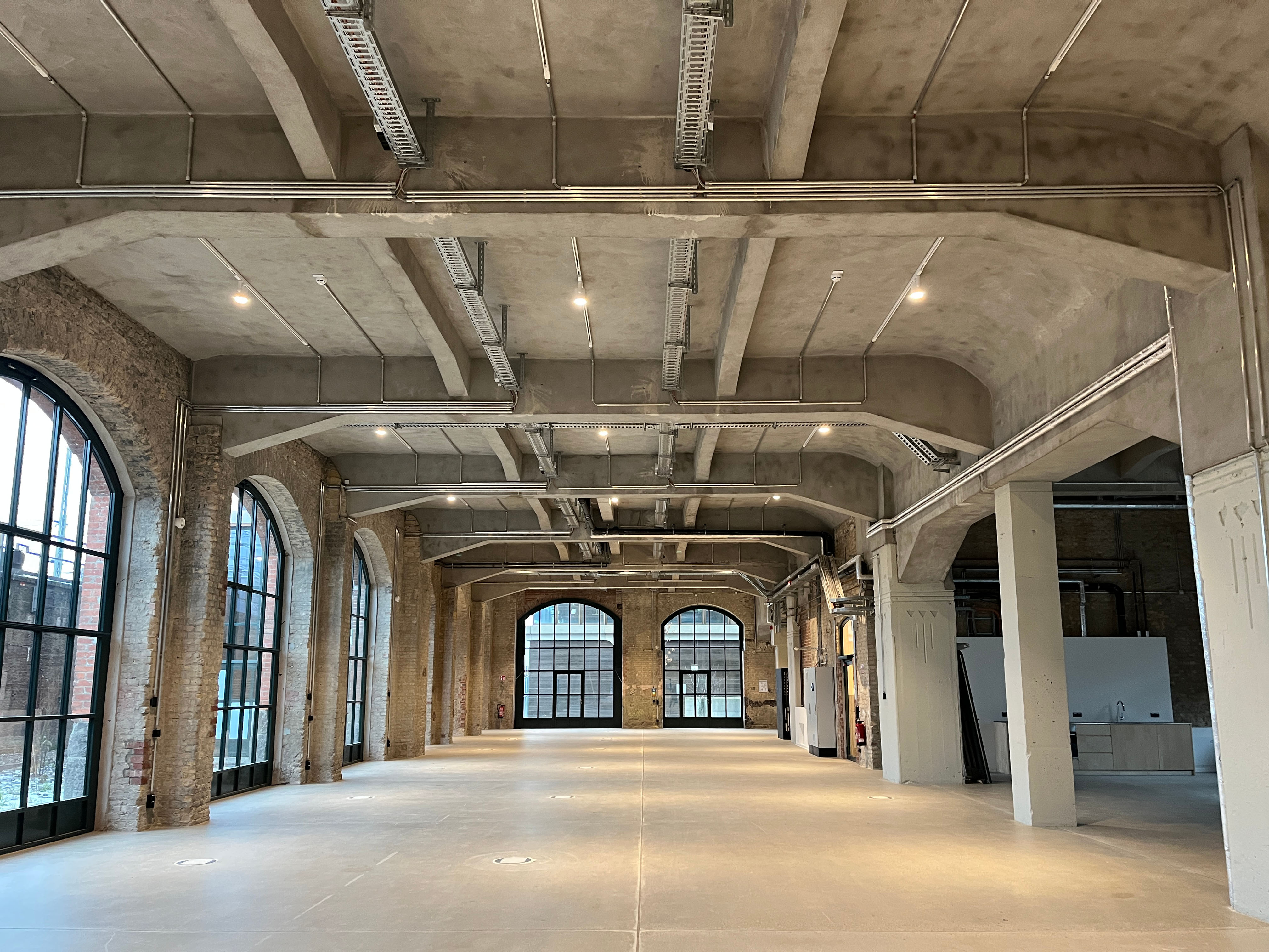 The construction progress at Postbahnhof Berlin shows the Abgangspackkammer on the ground floor with a spacious, empty interior, arched openings, columns, and even daylight.