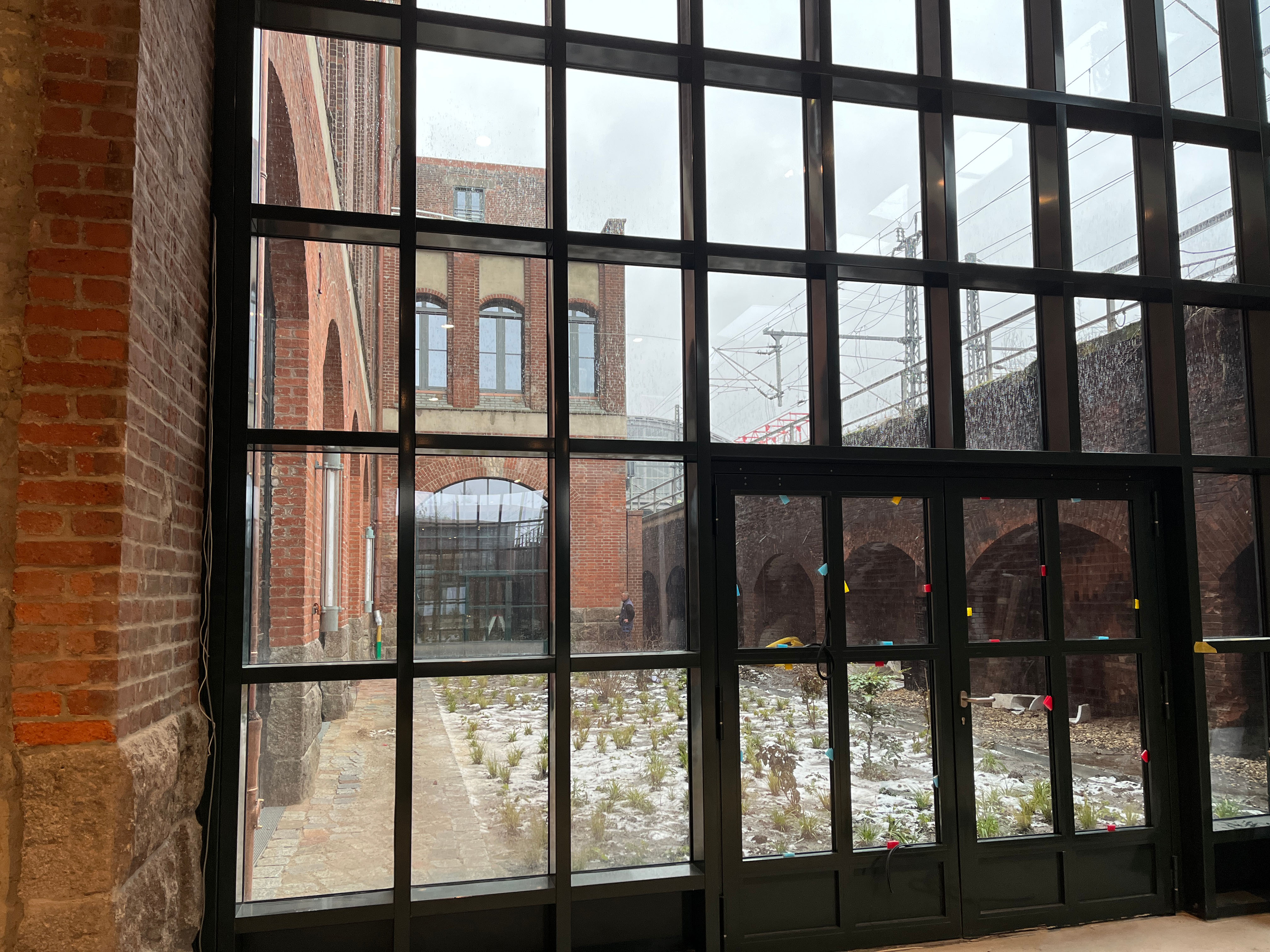 The construction progress at Postbahnhof Berlin shows the Abgangspackkammer on the ground floor with a large mullioned window and a view into the courtyard and surrounding brick facades.