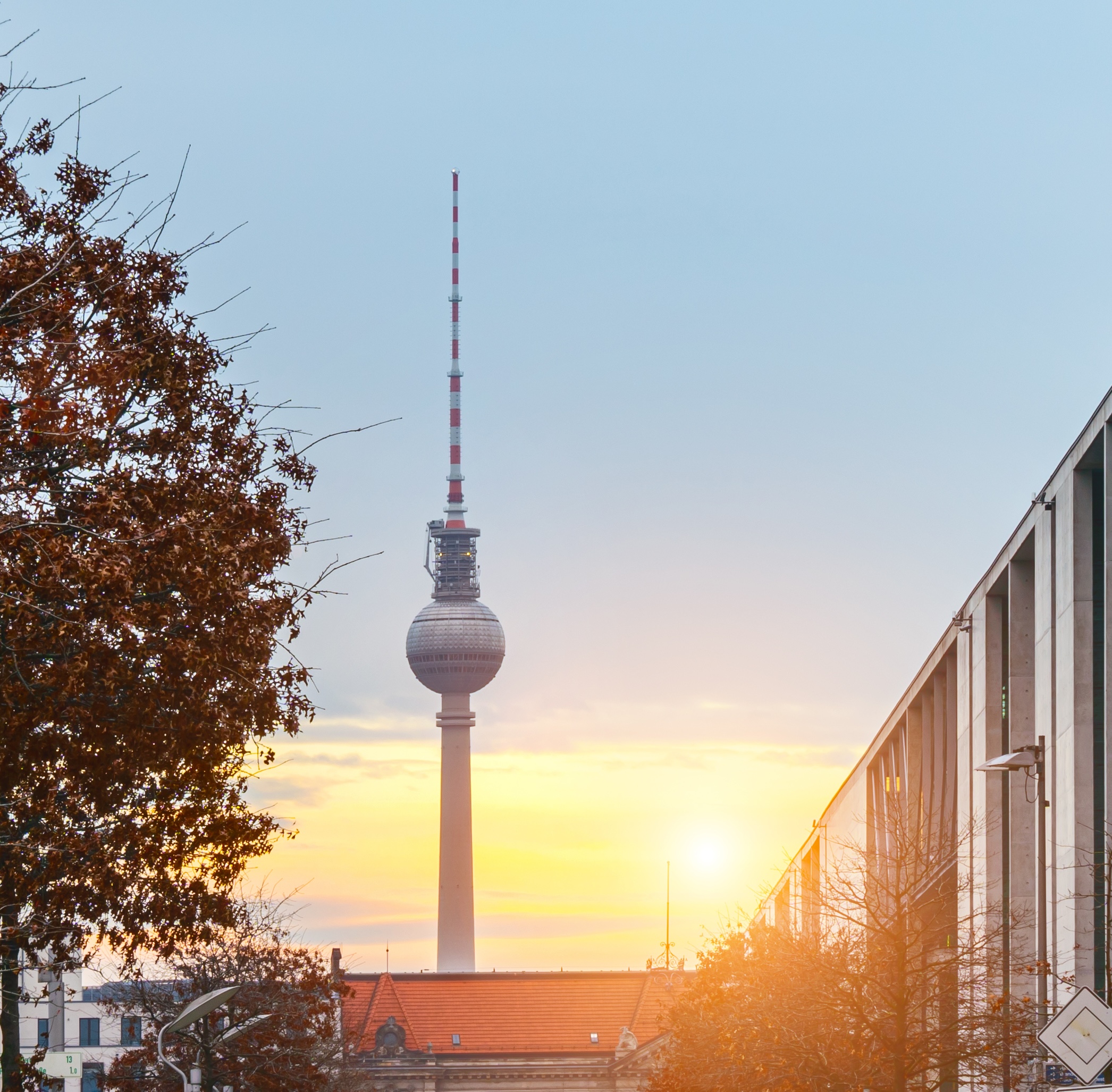 Der Berliner Fernsehturm bei Sonnenuntergang mit Bäumen im Vordergrund.