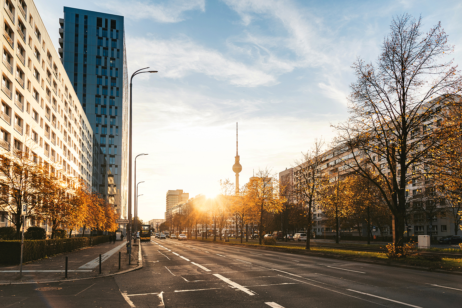 Sonnenuntergang in Berlin mit Bäumen entlang der Straße und modernen Gebäuden.