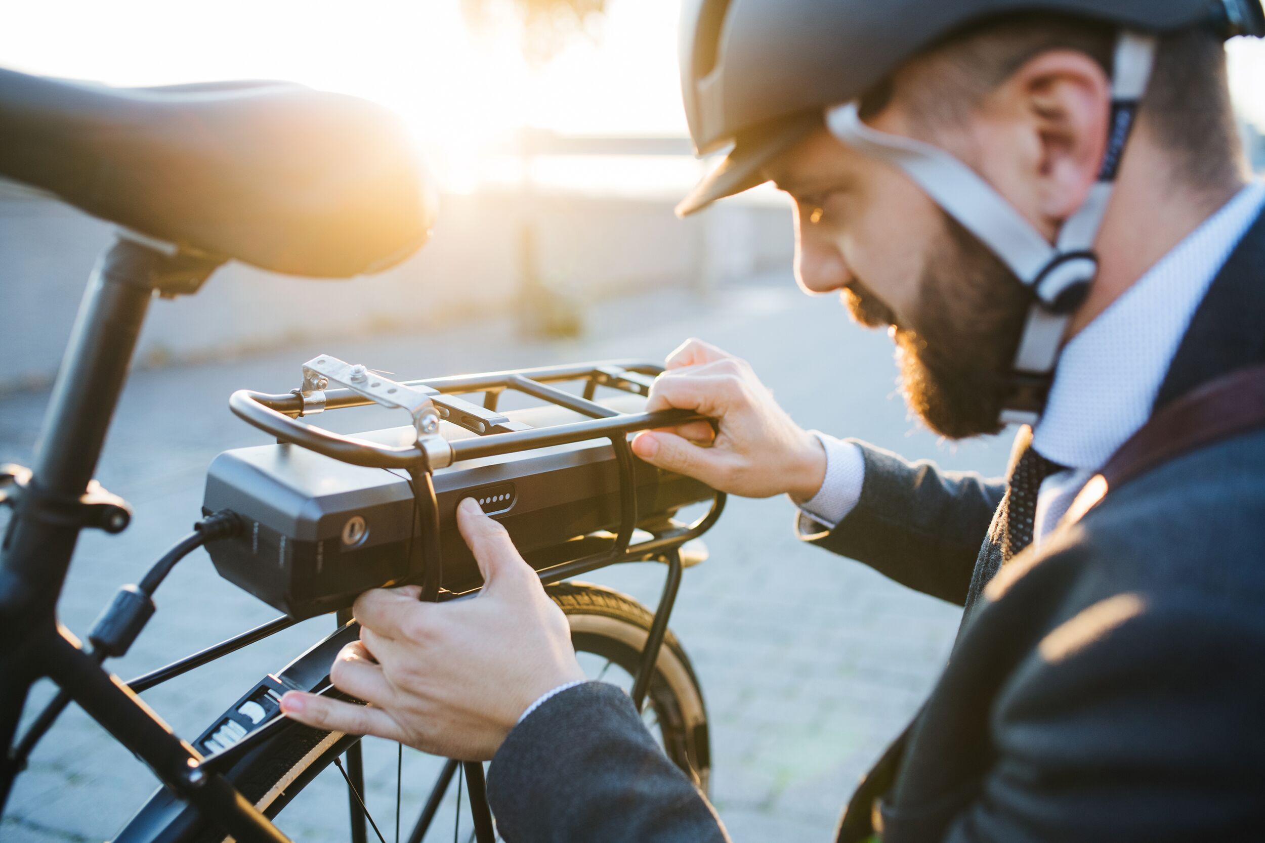 Geschäftsmann mit Helm beim Aufladen seines E-Bikes.